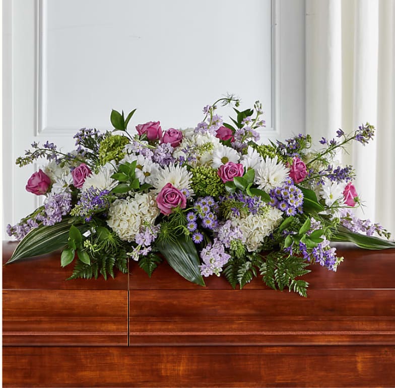 Casket spray with pink roses, white flowers, and purple accents