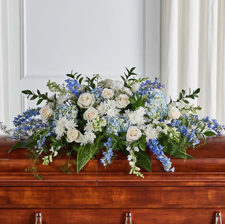 White and blue casket spray with roses and delphinium on a wooden casket