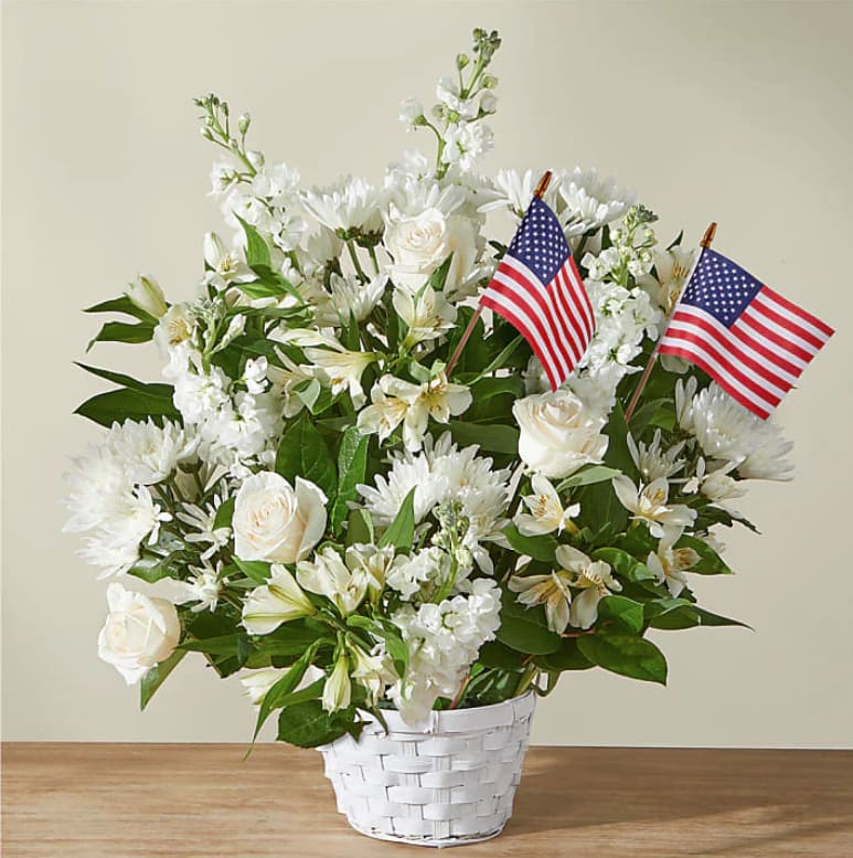 White floral arrangement in a white basket with two small American flags