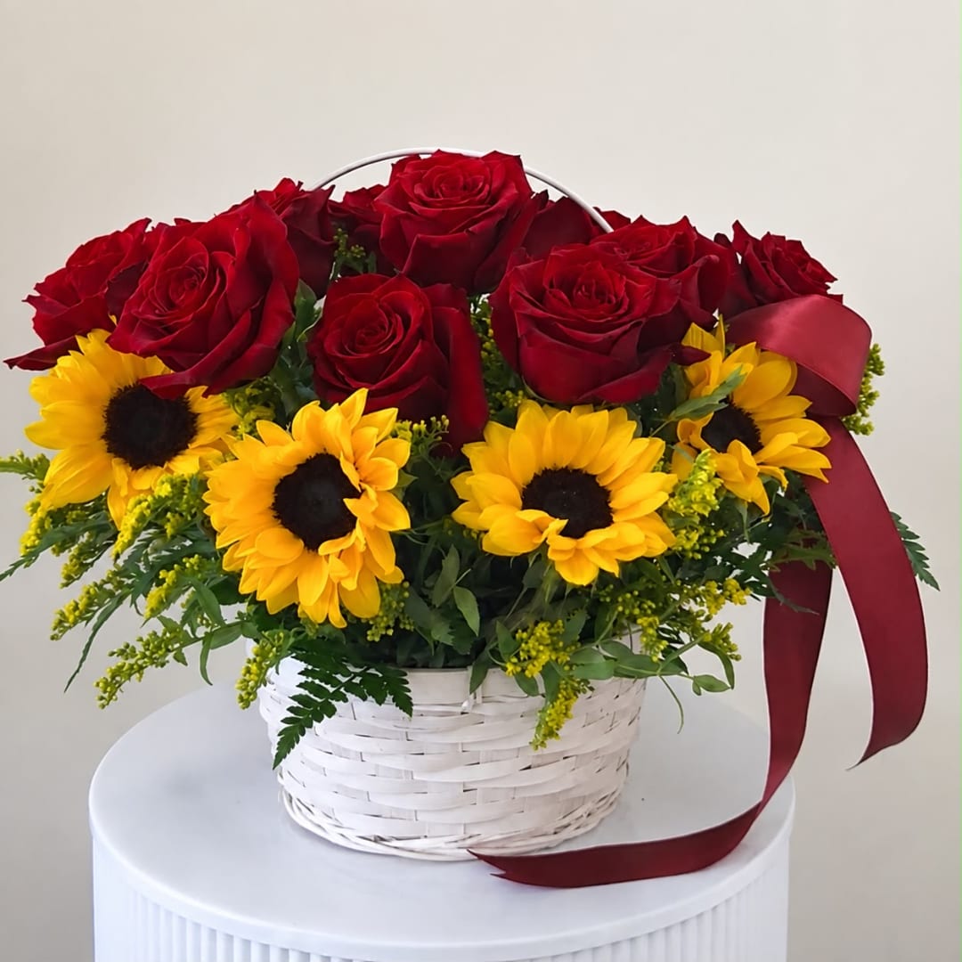 Red roses and yellow sunflowers in a white basket with a burgundy ribbon