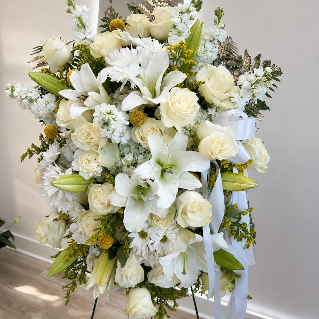 White floral standing spray with roses, lilies, and daisies on a ribboned easel