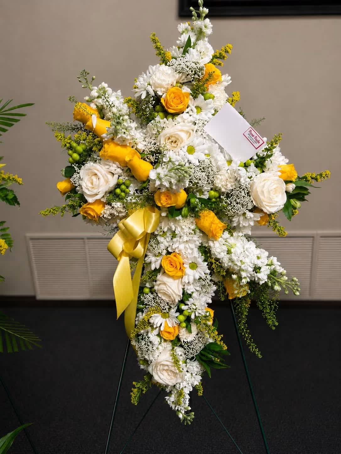 Cross-shaped floral spray with white and yellow flowers on a stand