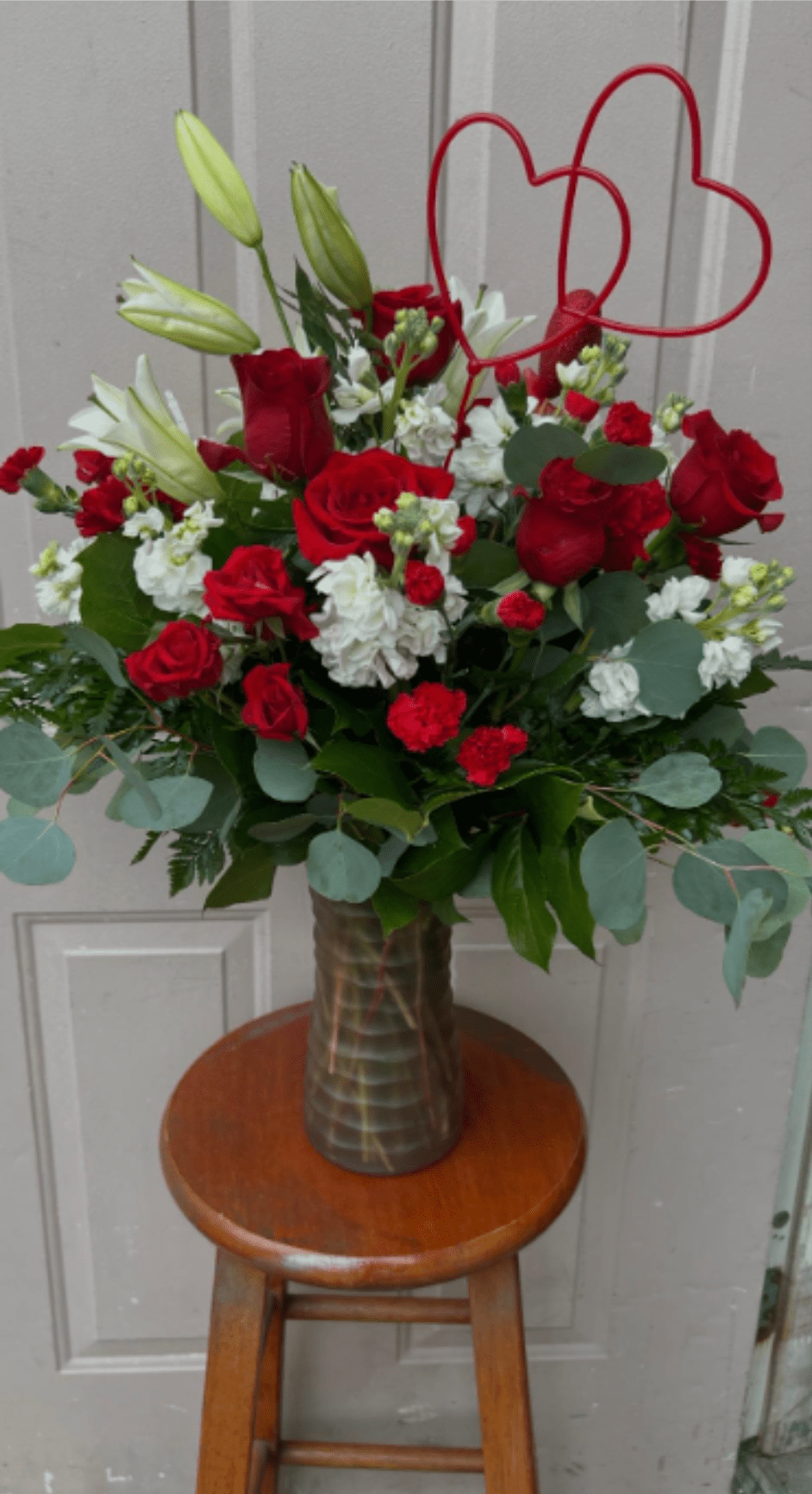 Red roses and white lilies in a tall vase with a red heart topper
