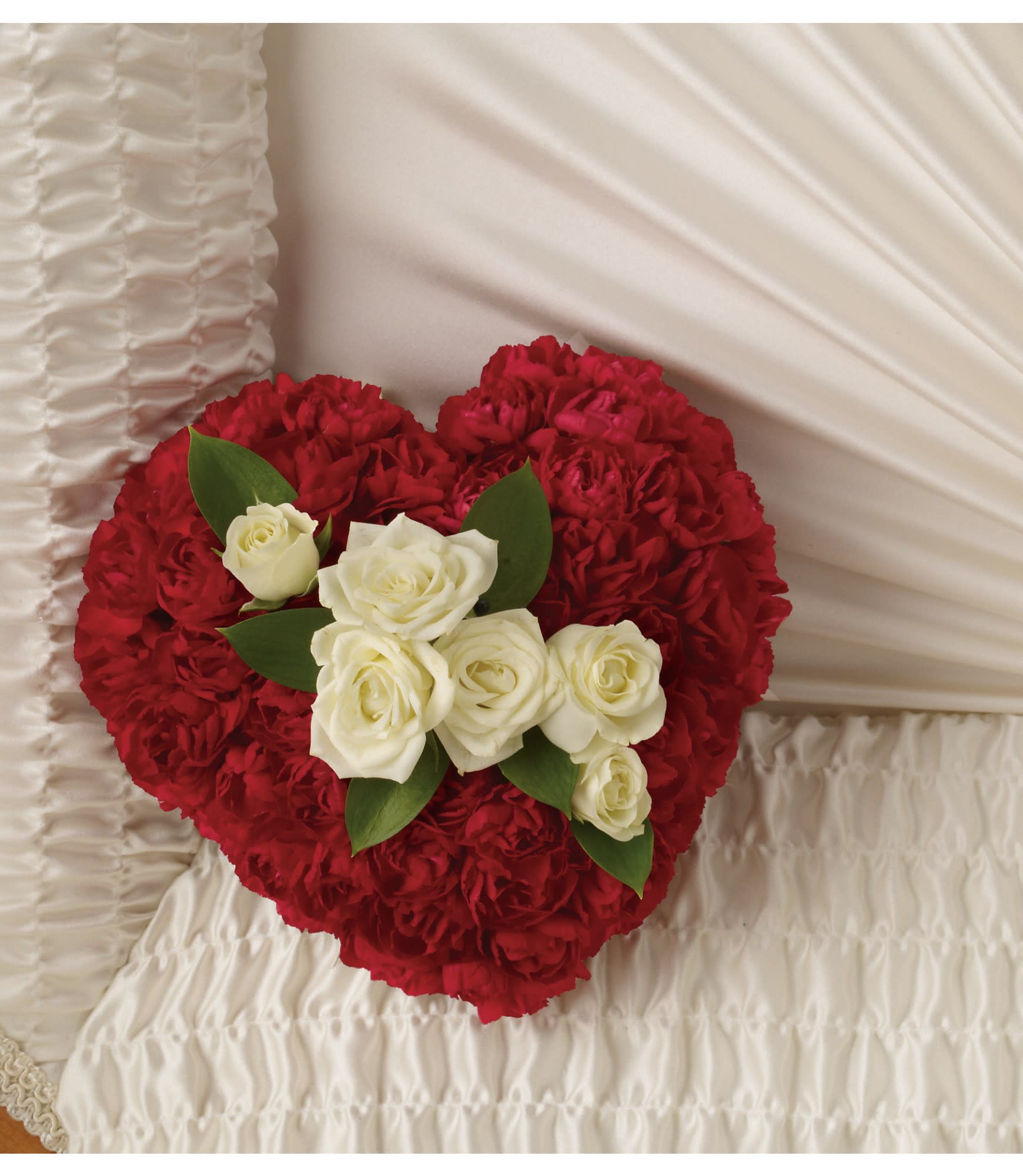 Heart-shaped arrangement of red carnations and white roses on white fabric