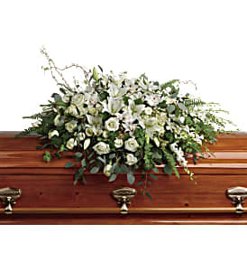 White lily and rose casket spray arranged on a polished wooden casket