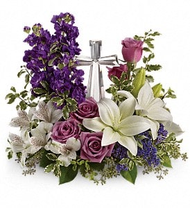 Low arrangement of white lilies and purple roses with a silver cross in the center
