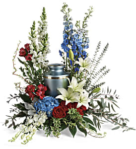 Cremation urn surrounded by red, white, and blue floral arrangement with tall blooms.