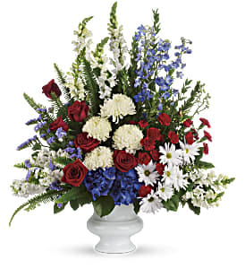 Tall red, white, and blue flower arrangement with roses and daisies in a white urn.