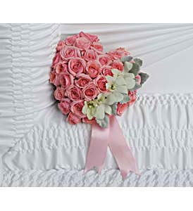 Heart-shaped pink rose arrangement with ribbon resting on white gathered fabric