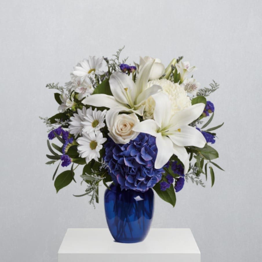 White lilies, blue hydrangea, and daisies arranged in a blue vase