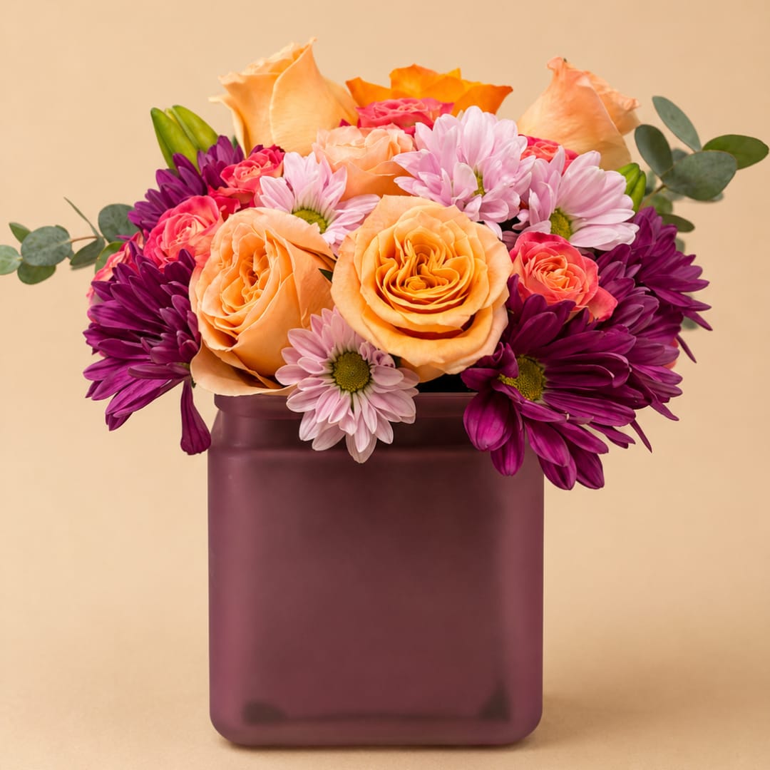 Peach roses and purple daisies in a square vase