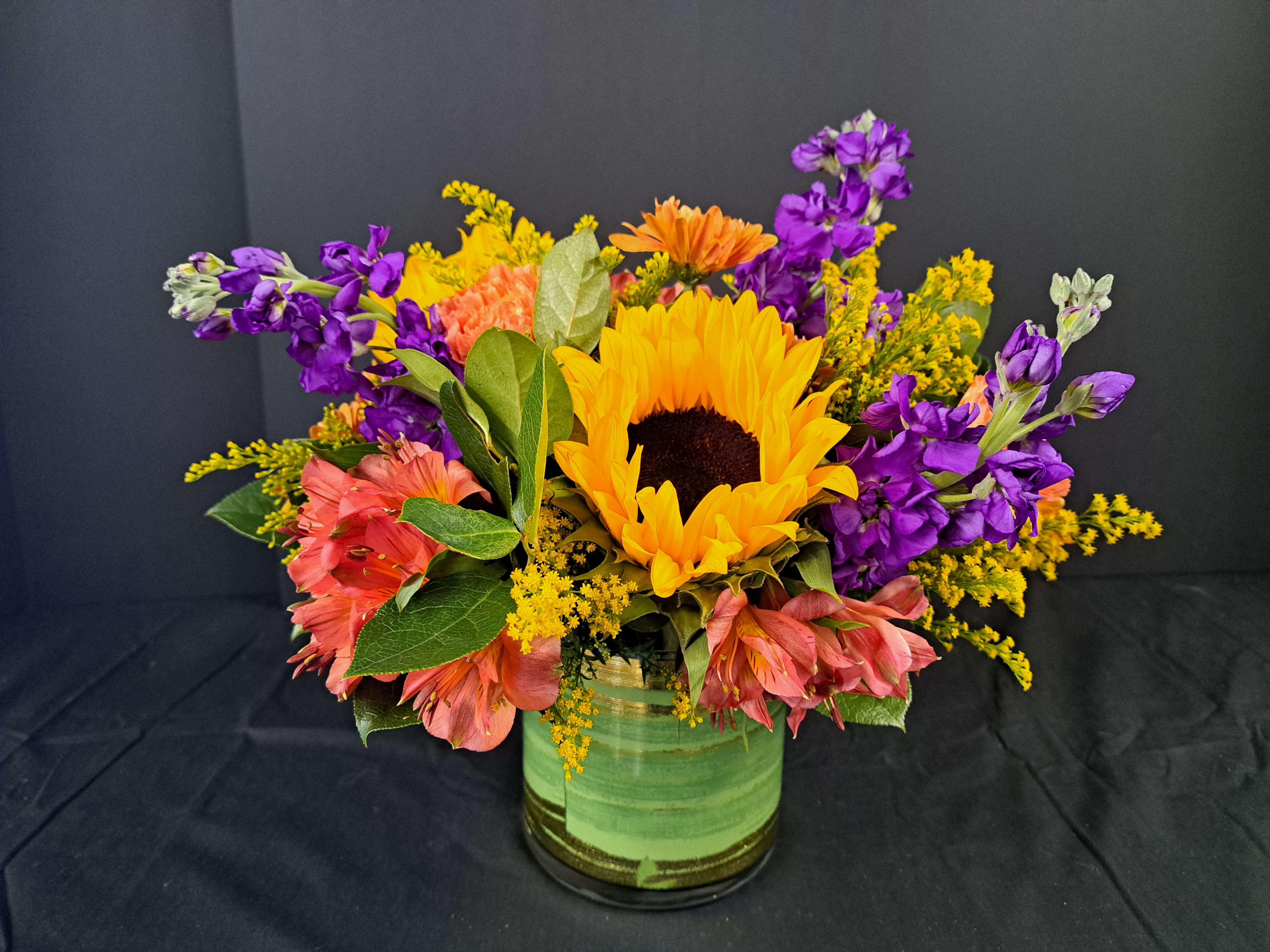 Sunflower bouquet with purple and pink flowers in a green glass vase