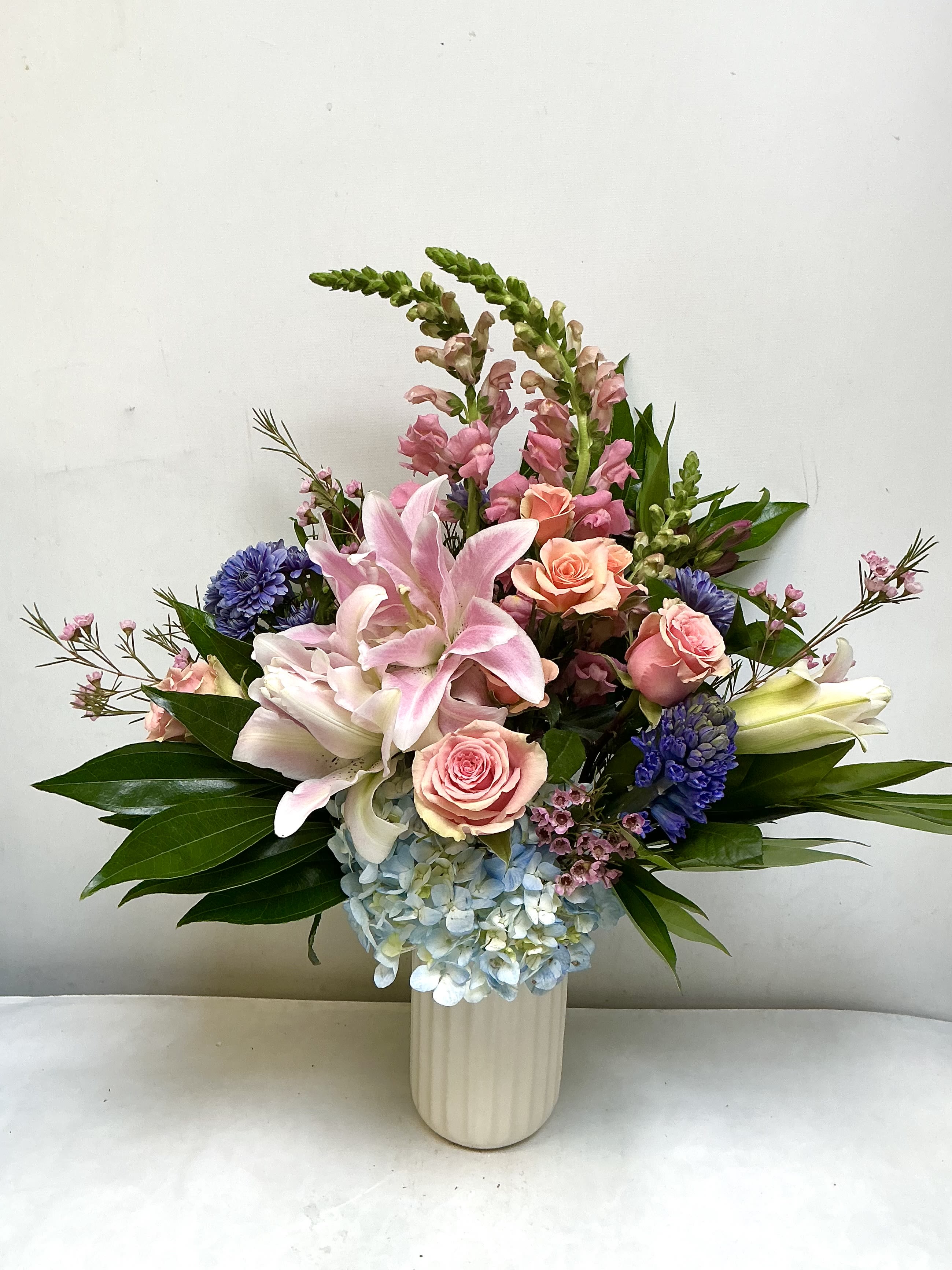 Grandma's Favorite - Large pink-and-white lilies take center stage in this flower arrangement, making it a perfect birthday bouquet or "thinking of you" gift for Grandma. The arrangement reads as a nostalgic, softly romantic tribute-she'll feel cherished the moment the lilies open and the fragrance fills the room. With pastel pinks and creamy whites balanced by blue and purple accents, it also suits Mother's Day, an anniversary, or a simple surprise to brighten her day.  Designed for everyday gifting, this composition celebrates comfort and warmth-ideal for the person who loves soft pastels and classic florals. Vase-ready on delivery; trim stems and refresh water every few days to extend bloom life and keep the arrangement looking its best.