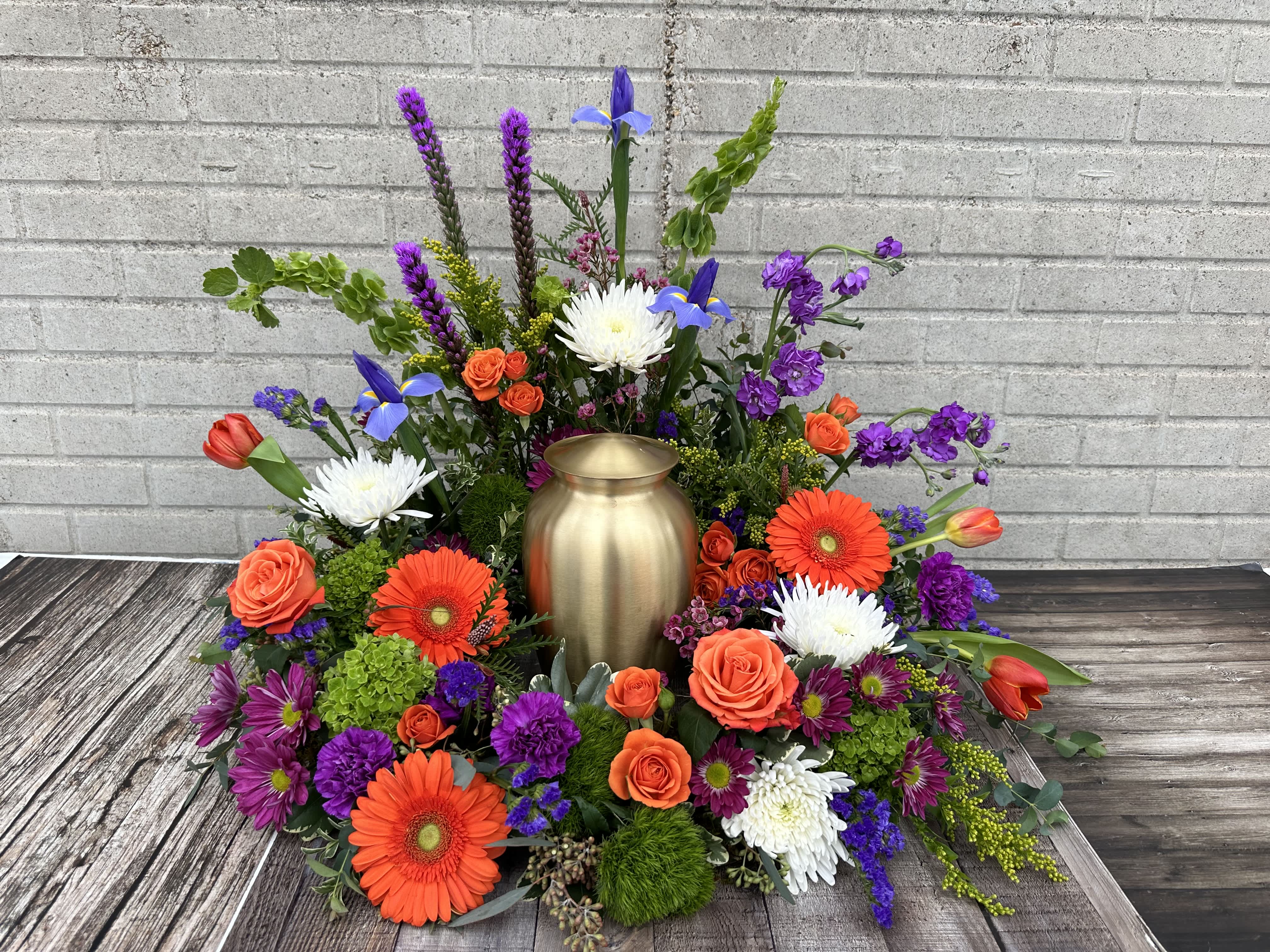 Colorful floral urn arrangement with orange roses, gerberas, and purple blooms