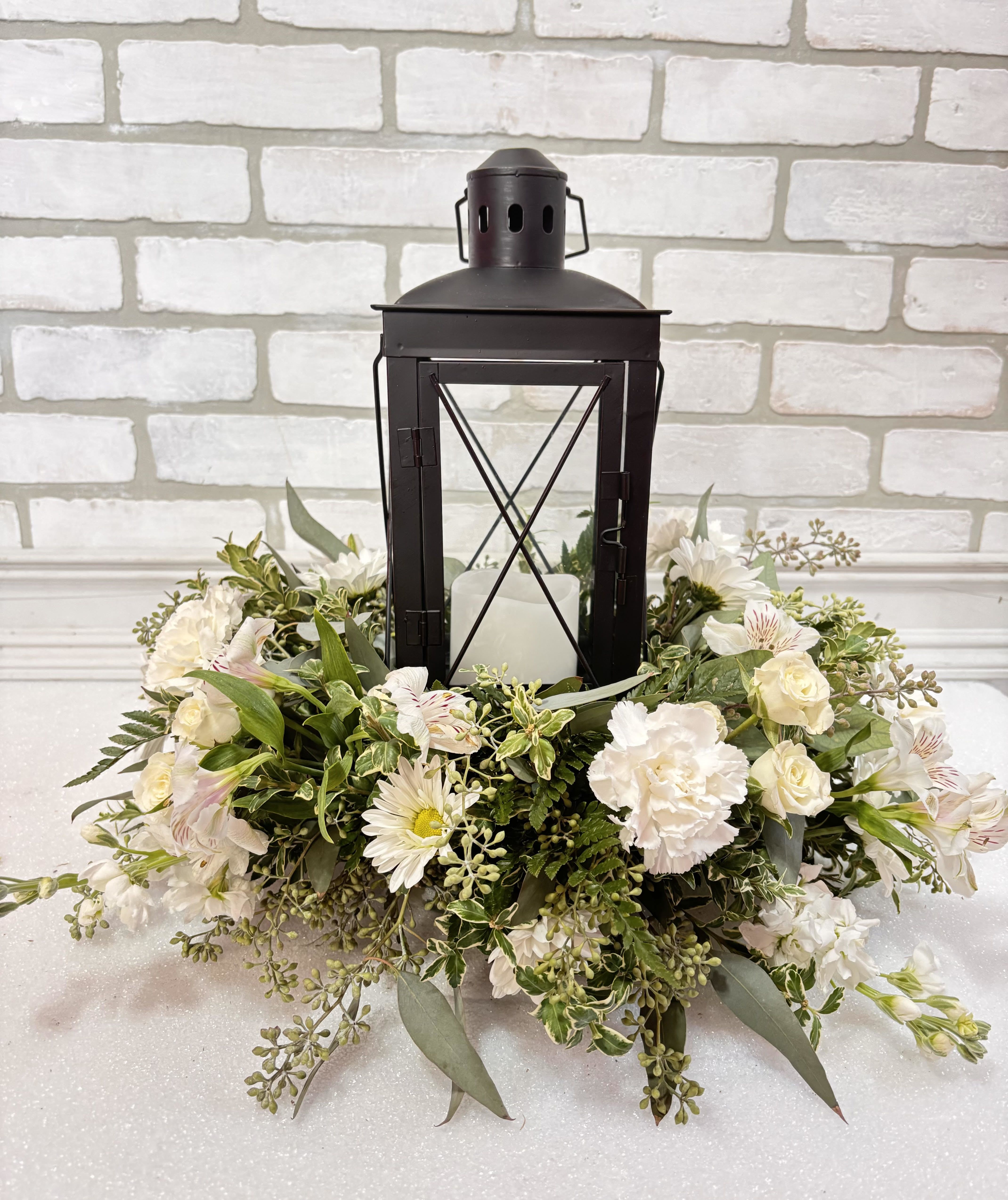 White floral wreath around a black lantern with a candle inside