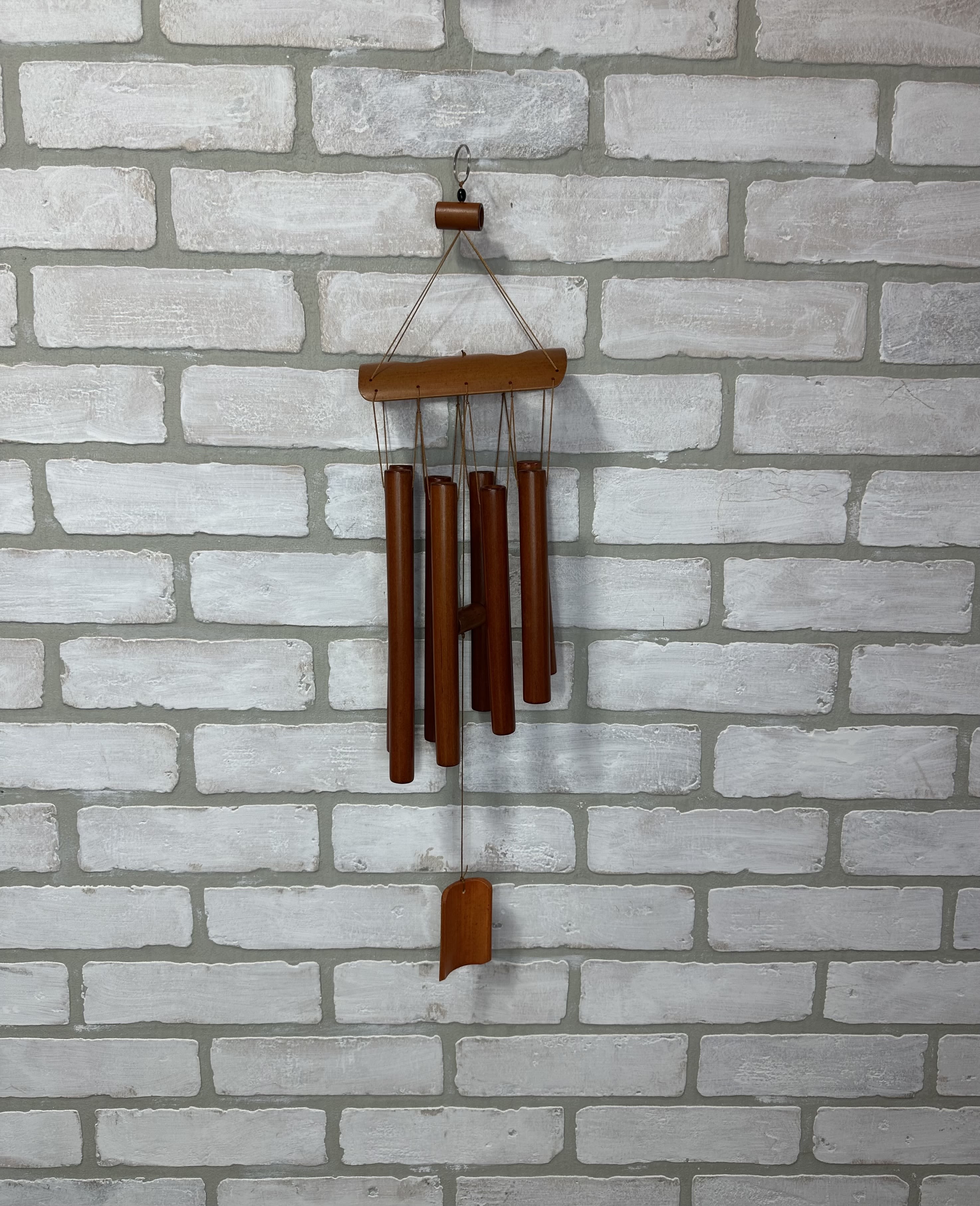 Wooden wind chime hanging on a white brick wall