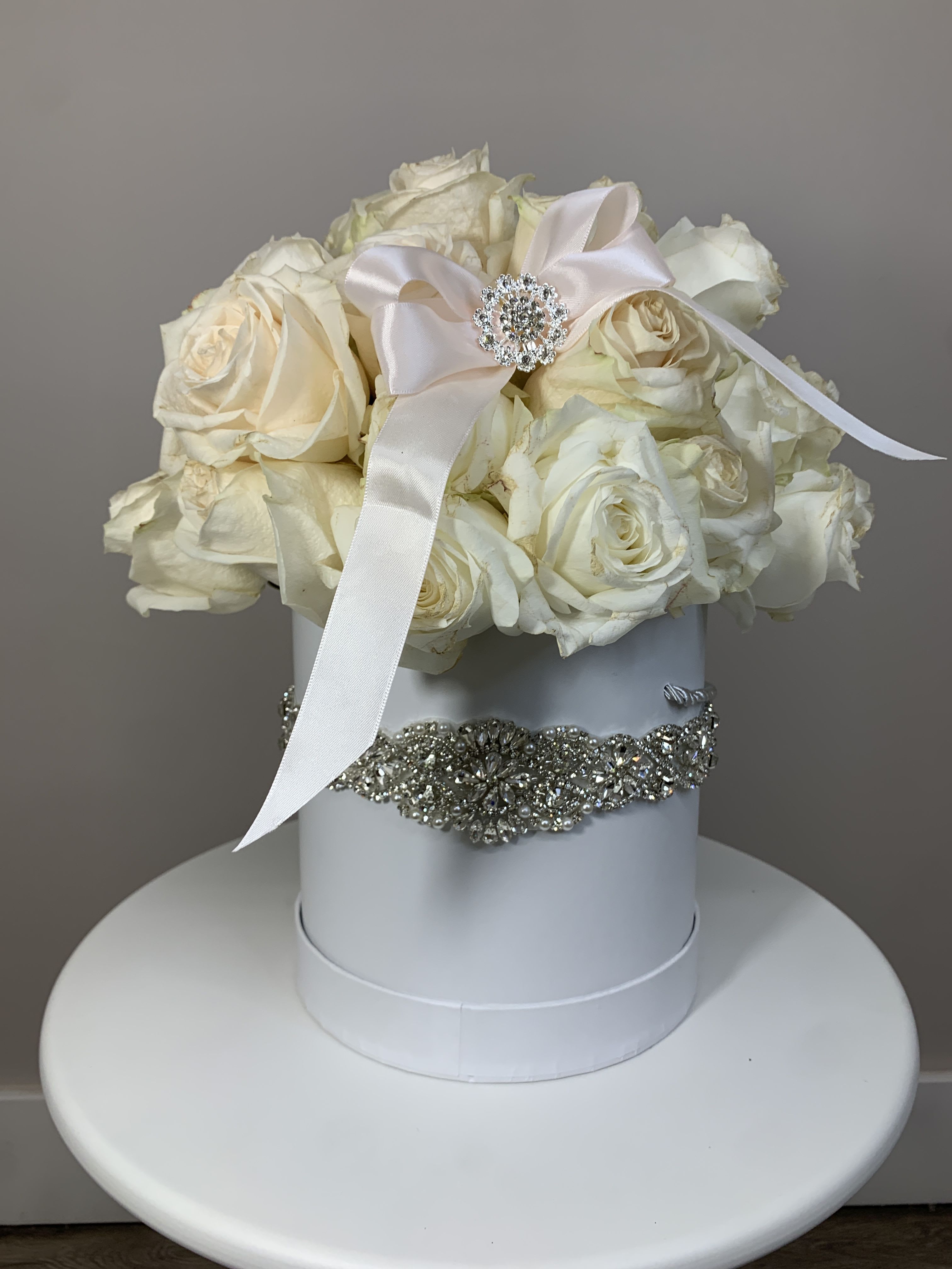 White roses arranged in a round hat box with a satin ribbon