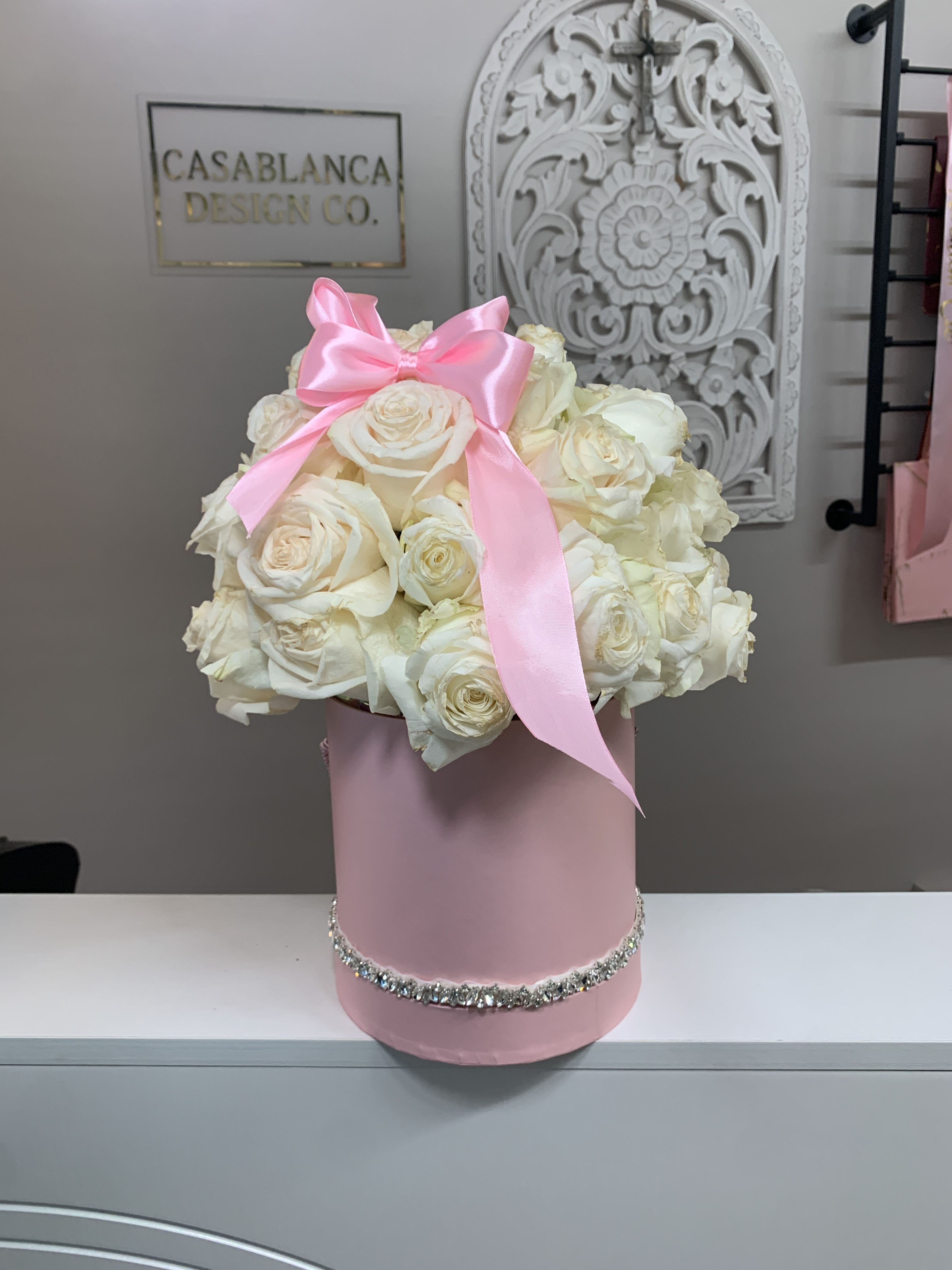 White rose arrangement in a pink hat box with a pink ribbon