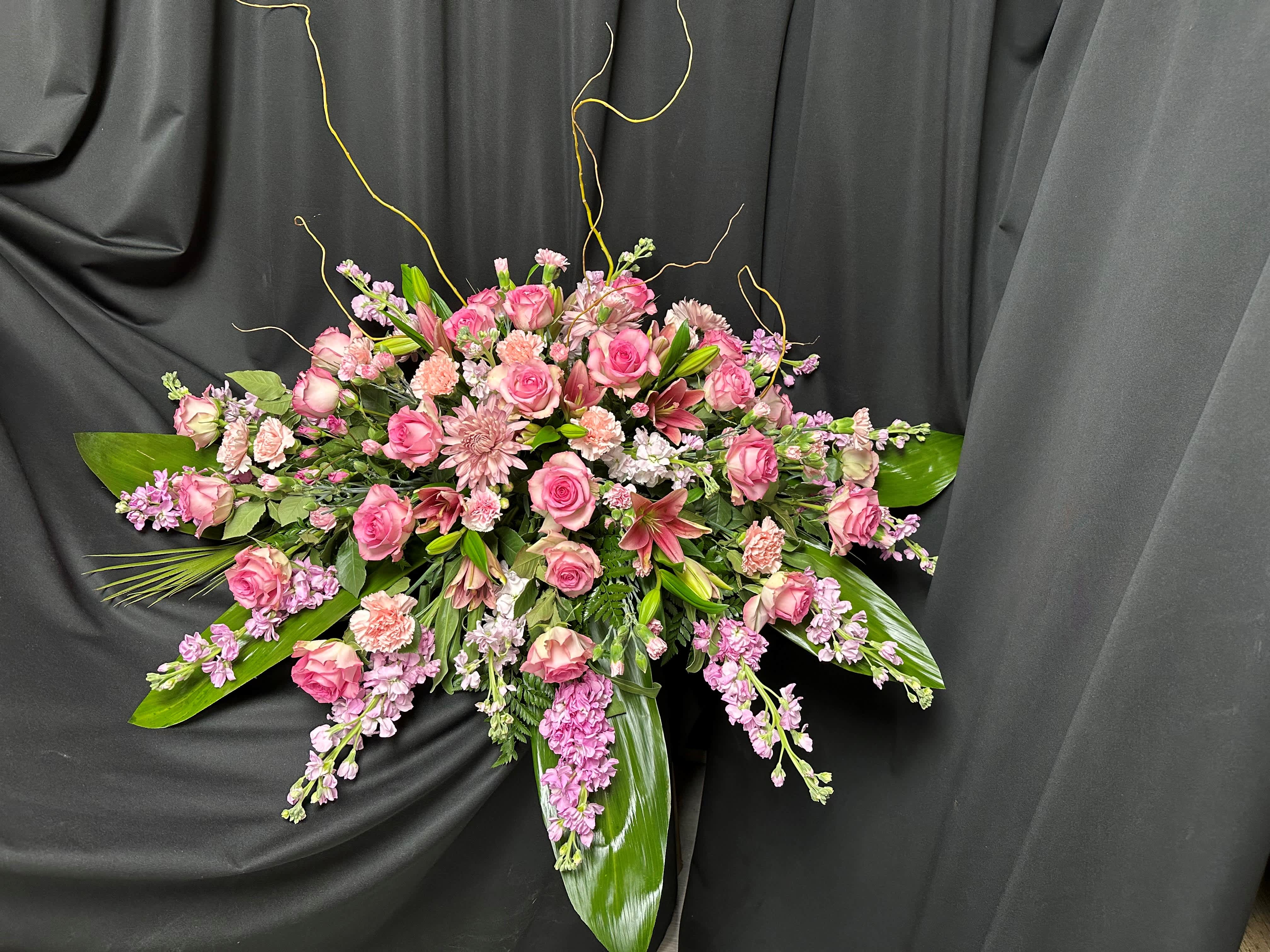 Pink roses and lilies arranged with trailing purple flowers on a black drape