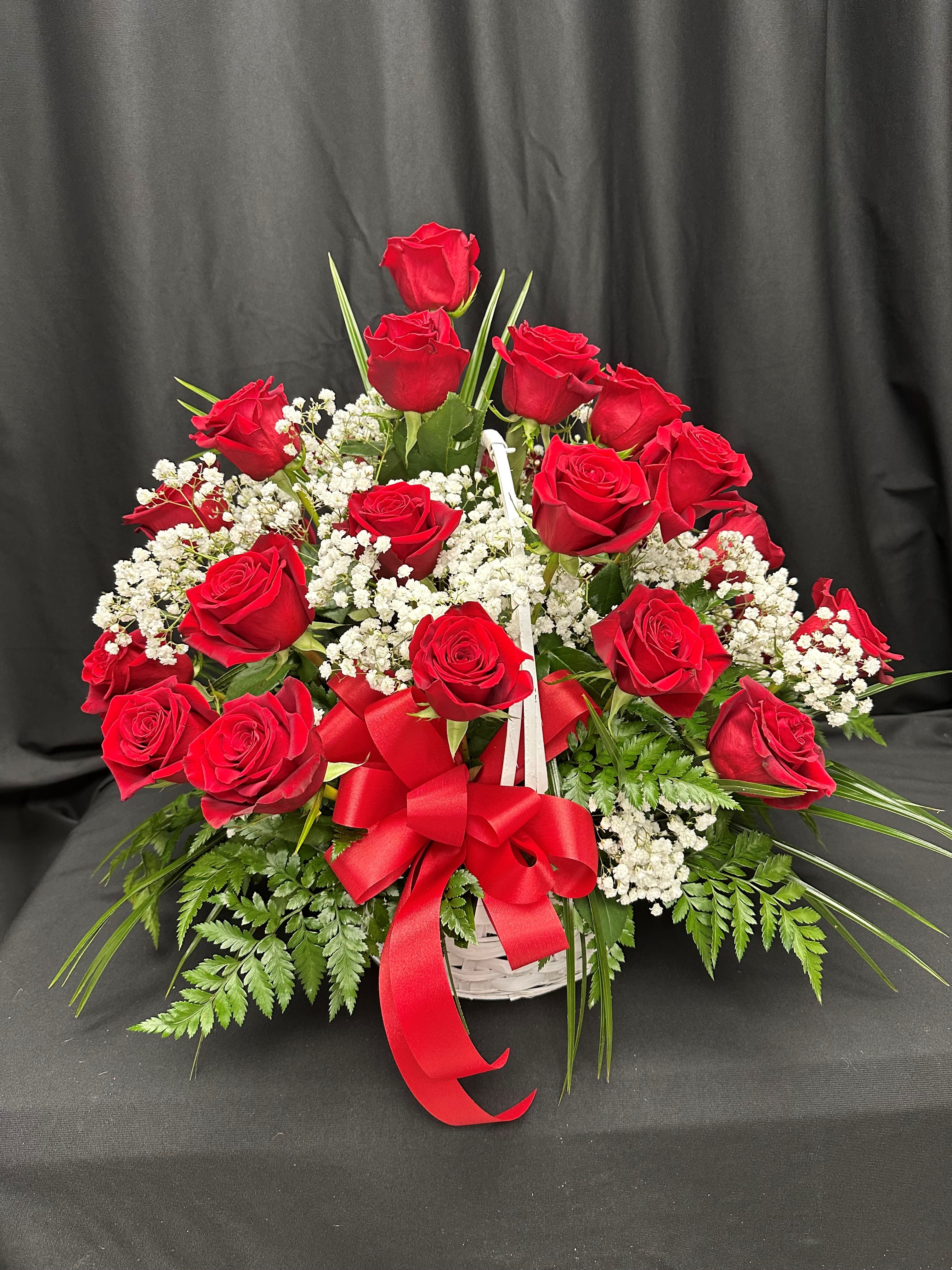 Red roses arranged in a white basket with baby's breath and a red ribbon