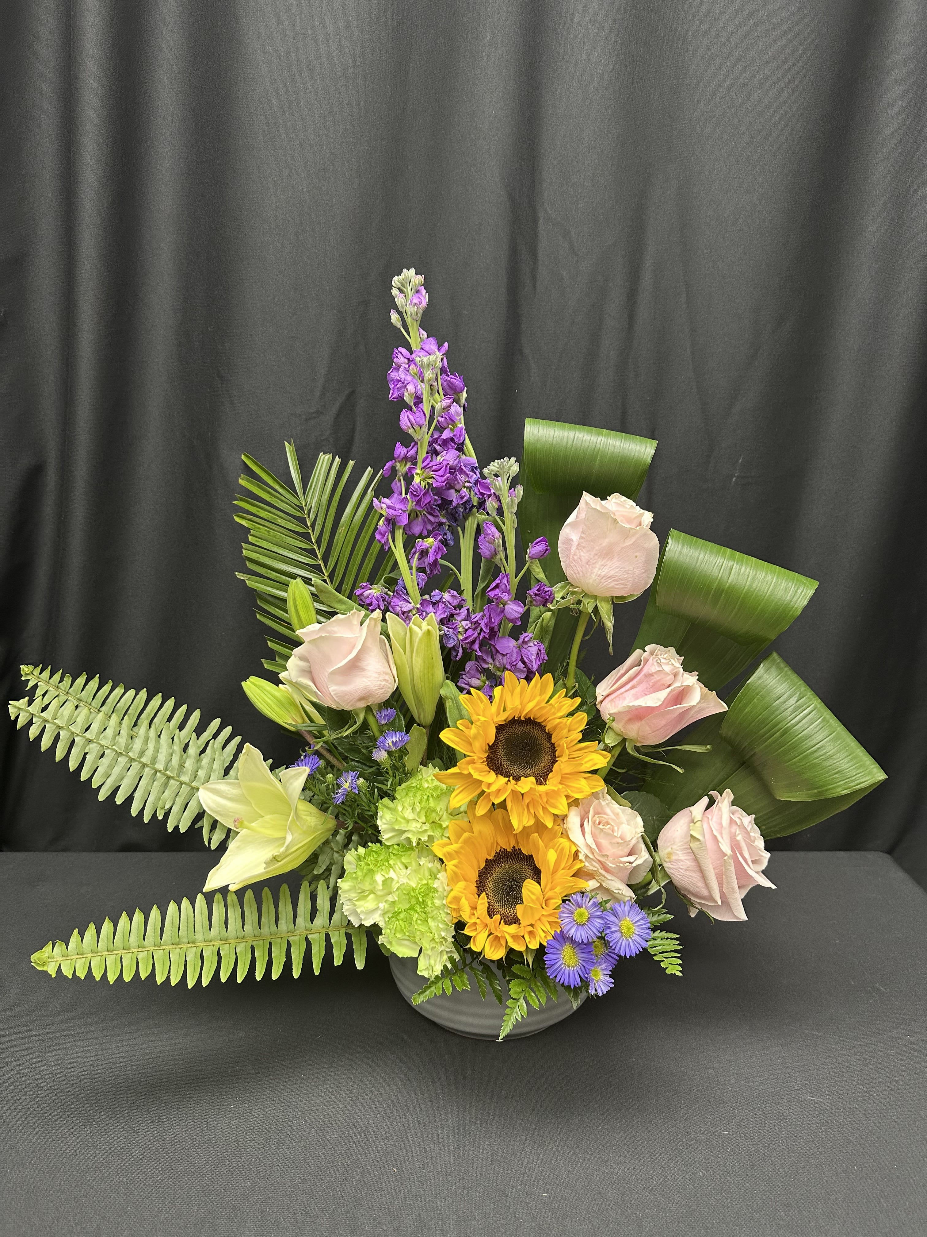 Mixed bouquet with pink roses, sunflowers, and purple flowers in a vase