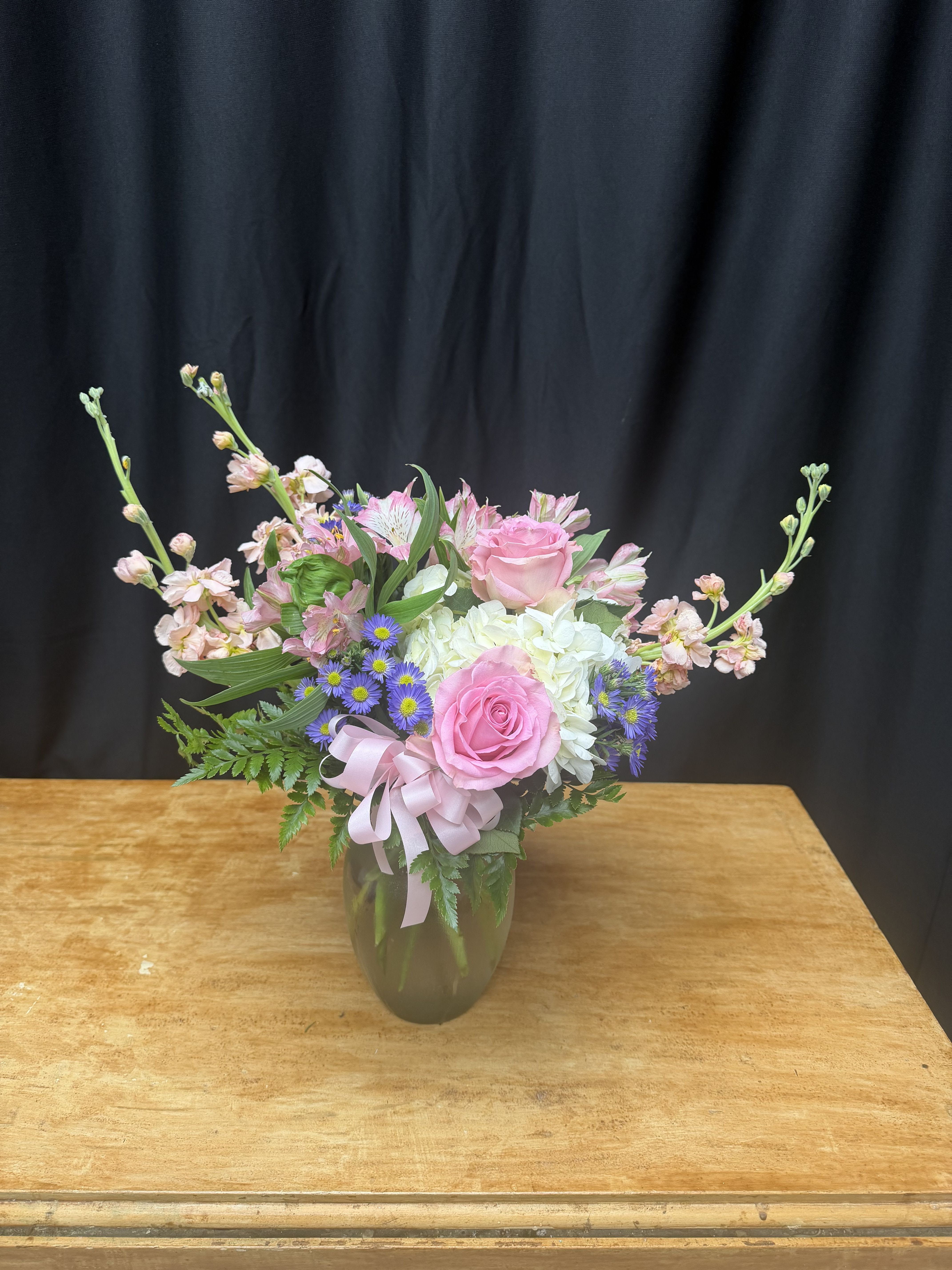 Pink roses and mixed flowers arranged in a glass vase with a ribbon