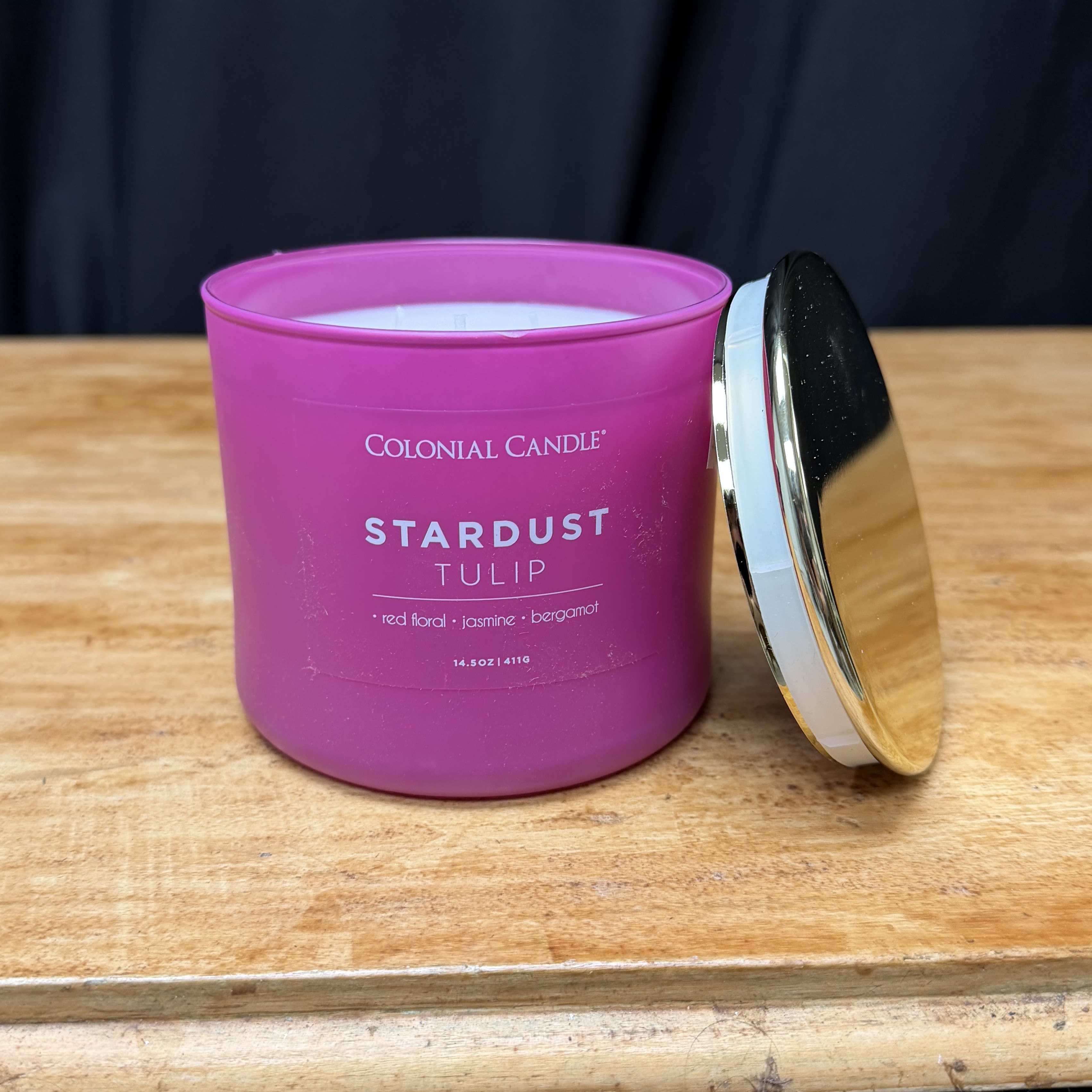 Pink candle in a glass jar with a metal lid on a wooden surface.