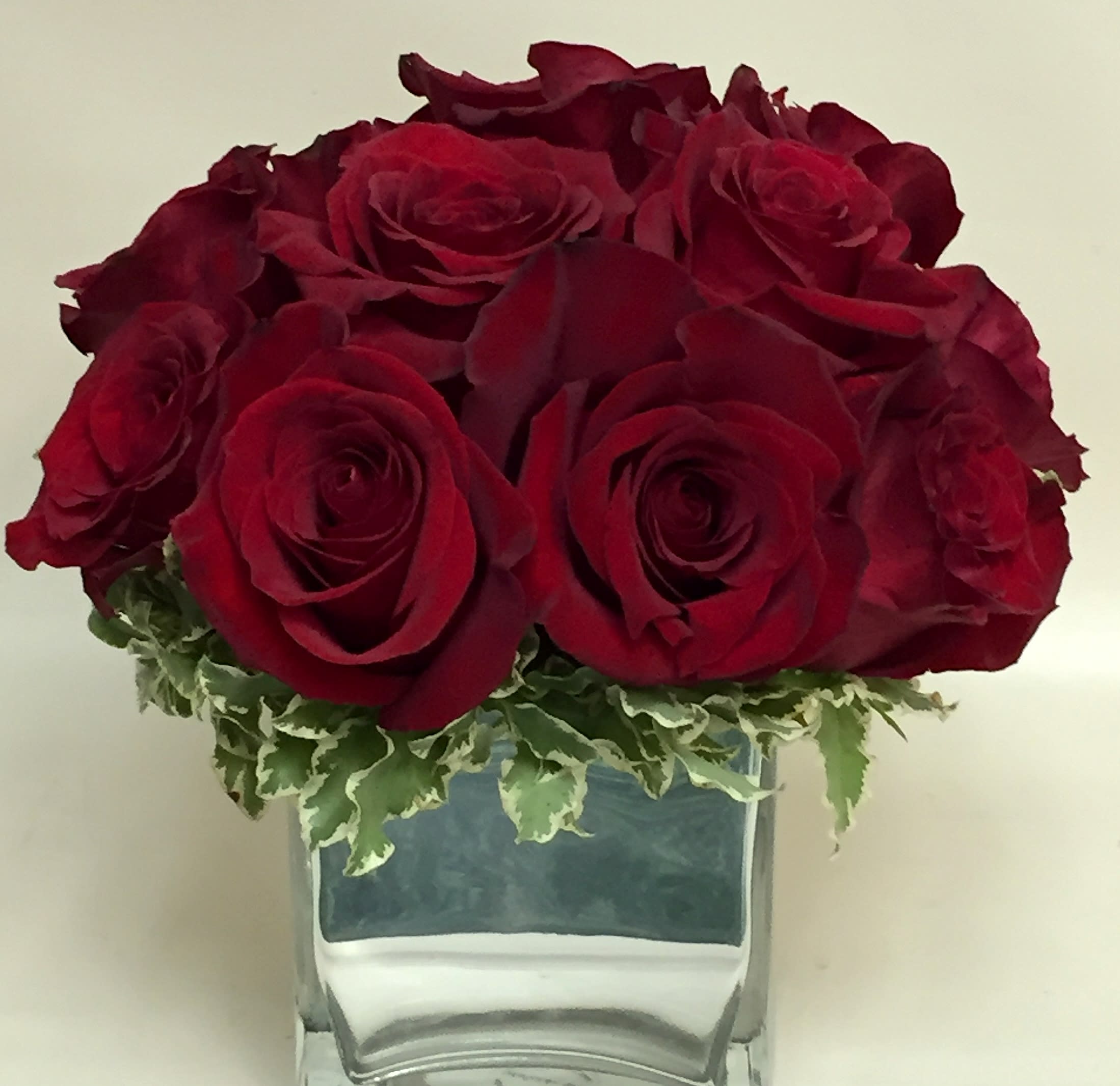 Red roses arranged in a clear glass vase with variegated greenery