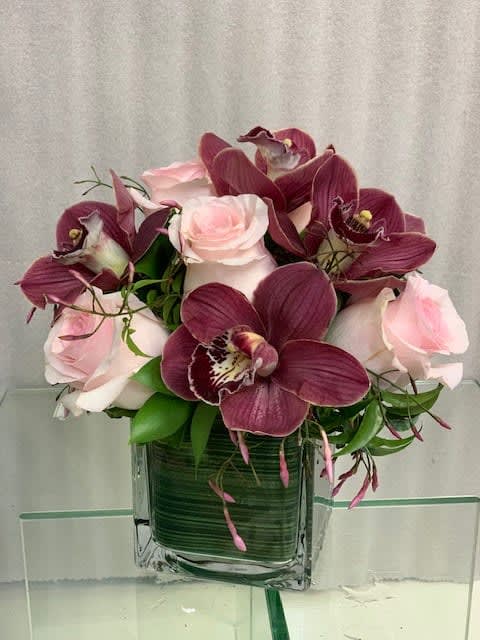 Pink roses and burgundy orchids in a square glass vase
