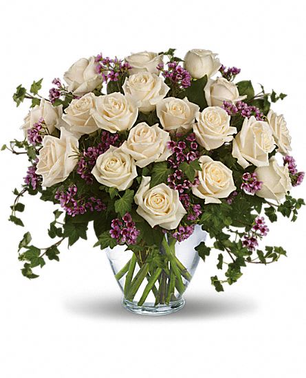 White roses and purple filler flowers in a clear glass vase