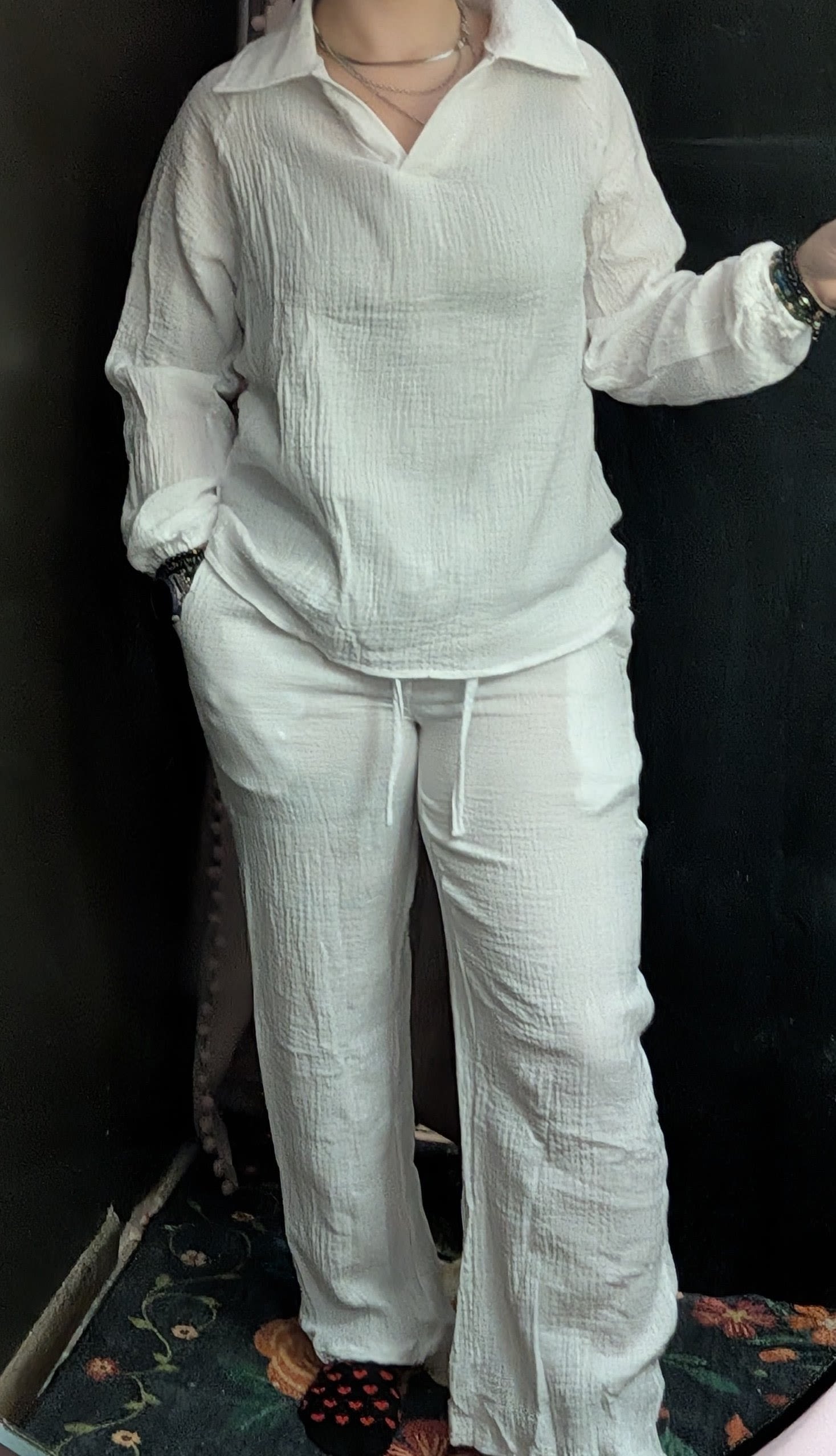 Person wearing a white textured shirt and pants against a dark background
