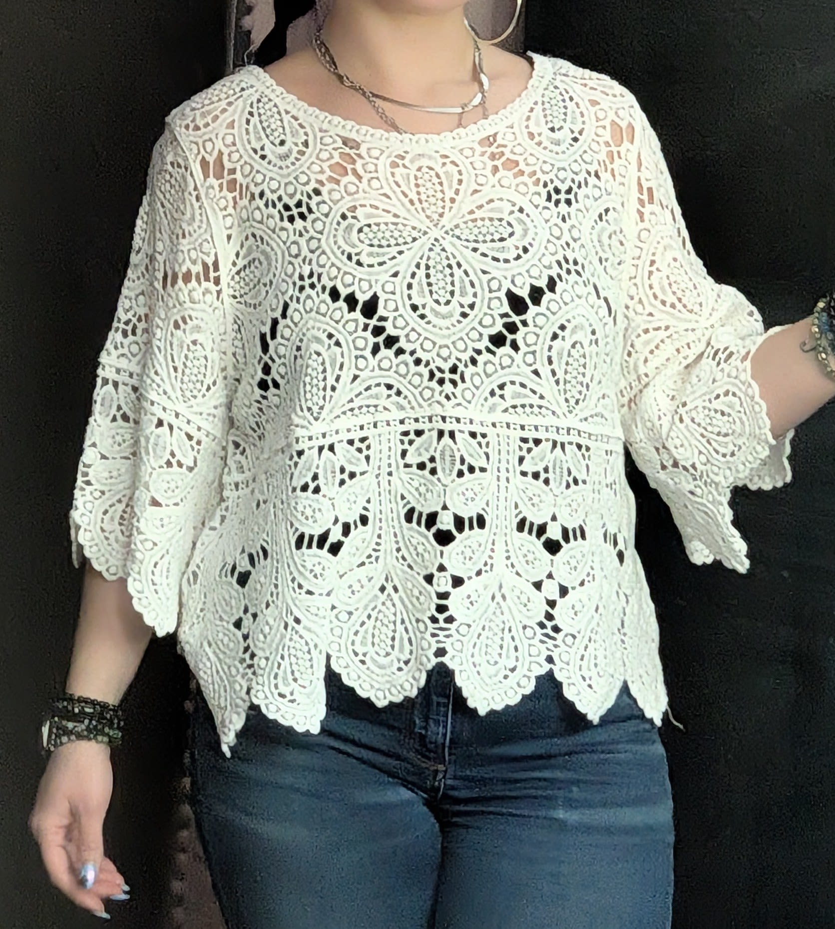 Person wearing a white lace top and blue jeans against a dark background