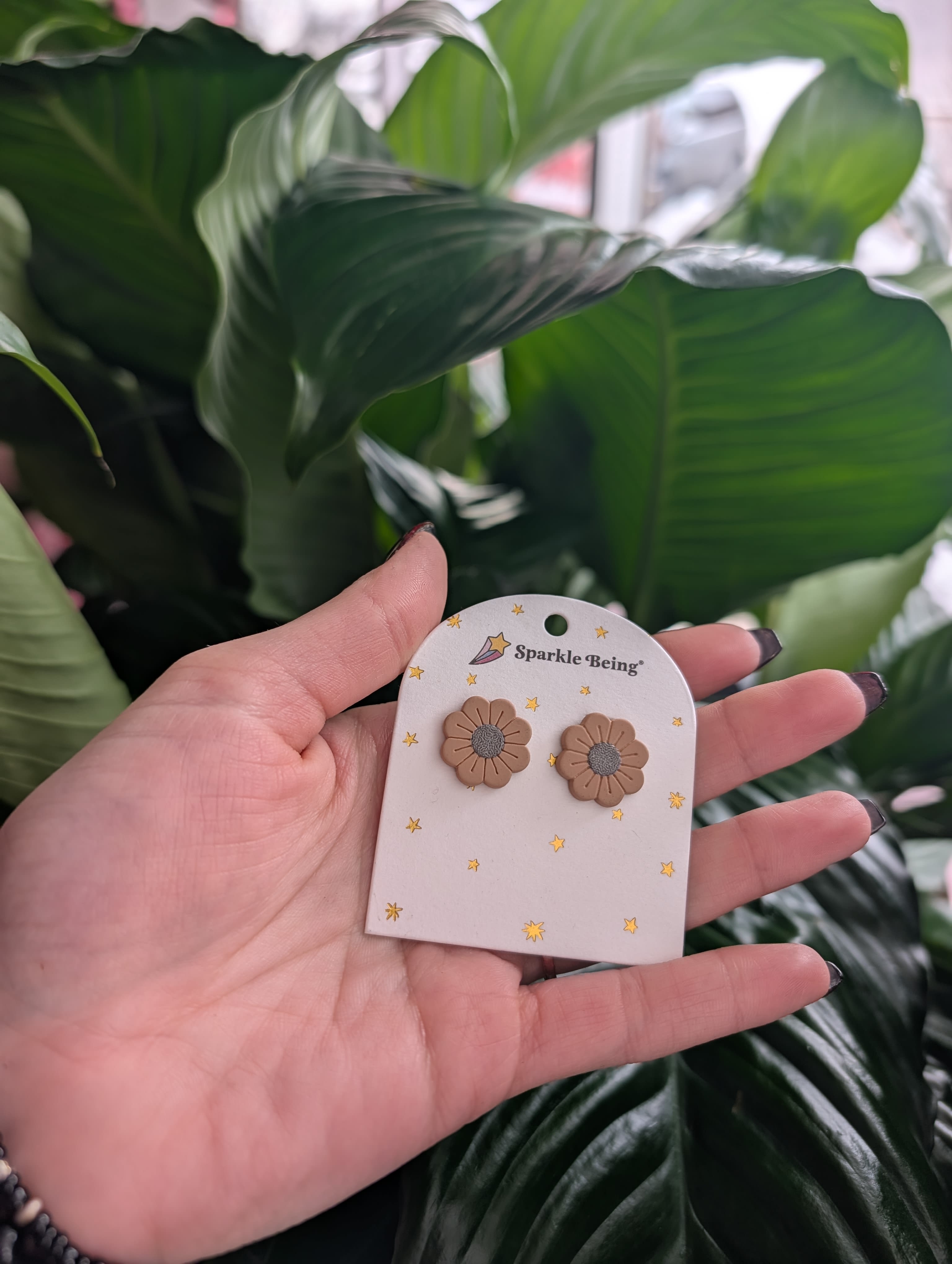 Hand holding daisy-shaped stud earrings on a card