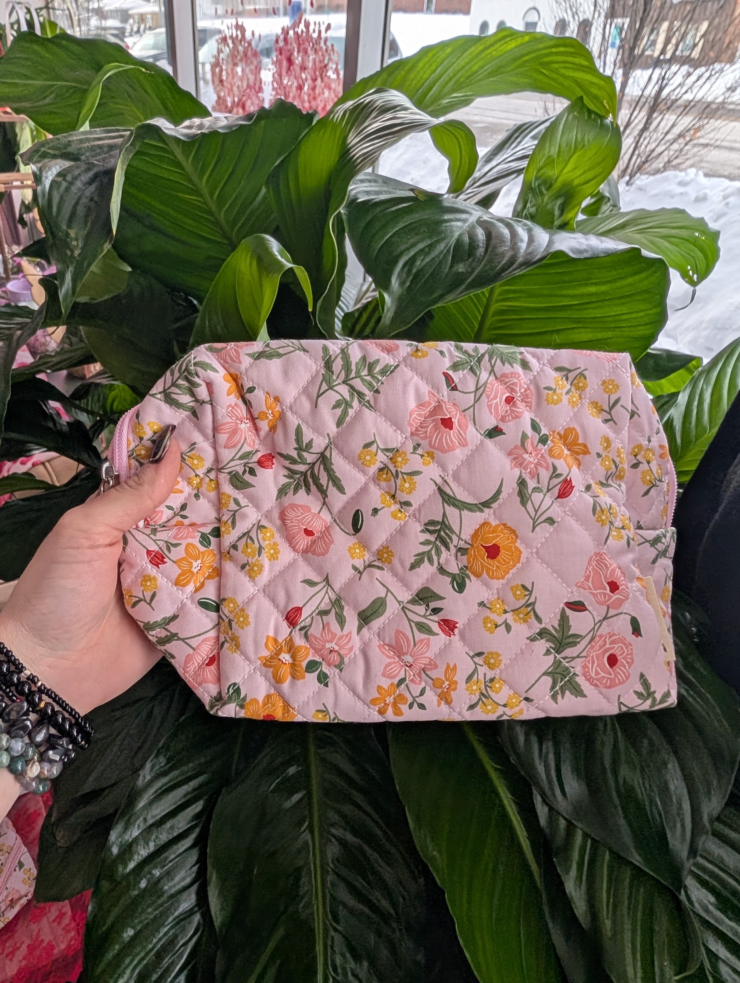 Pink floral quilted pouch held in front of large green houseplant leaves