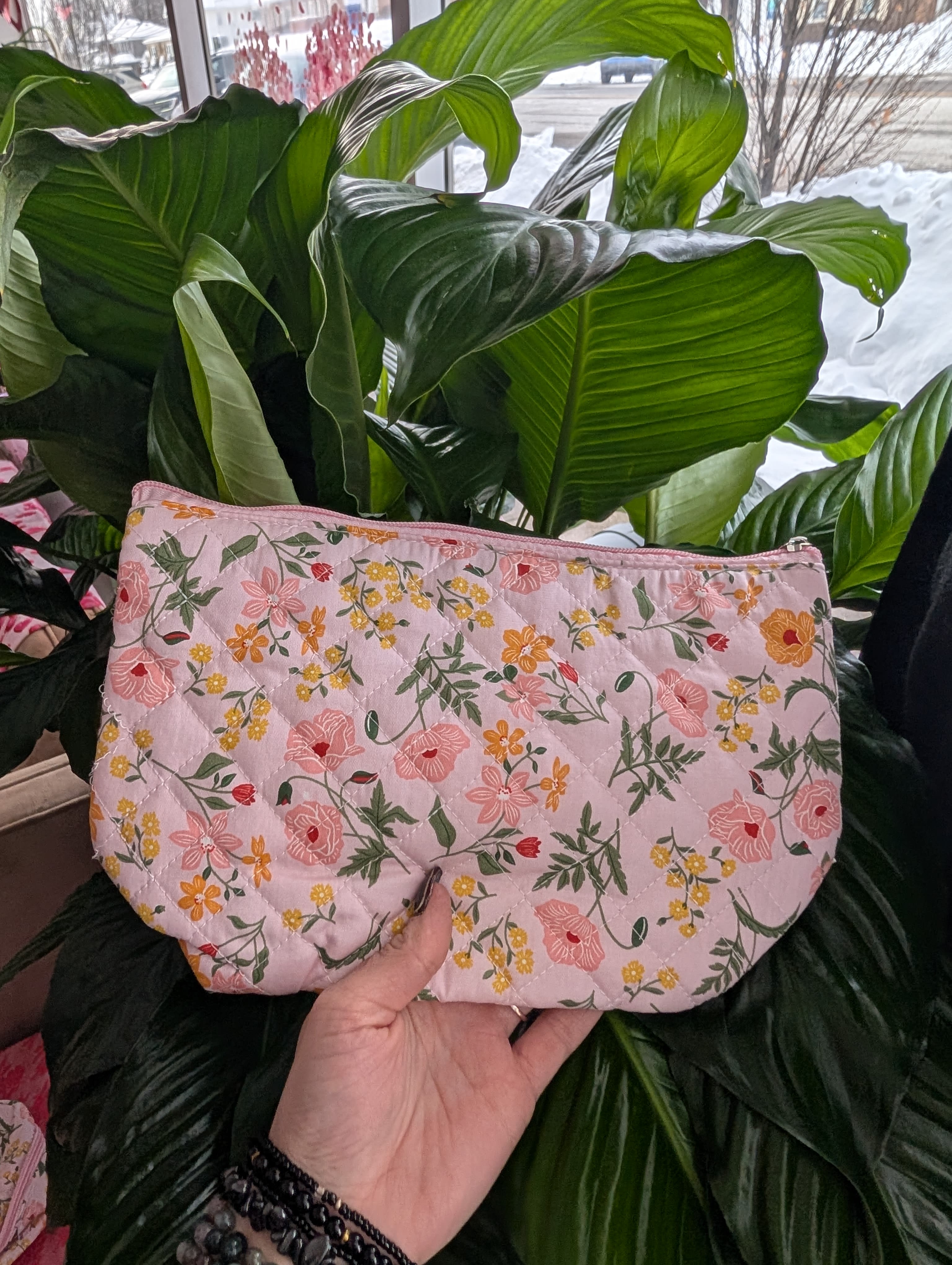 Pink quilted floral pouch held in front of large green houseplant leaves