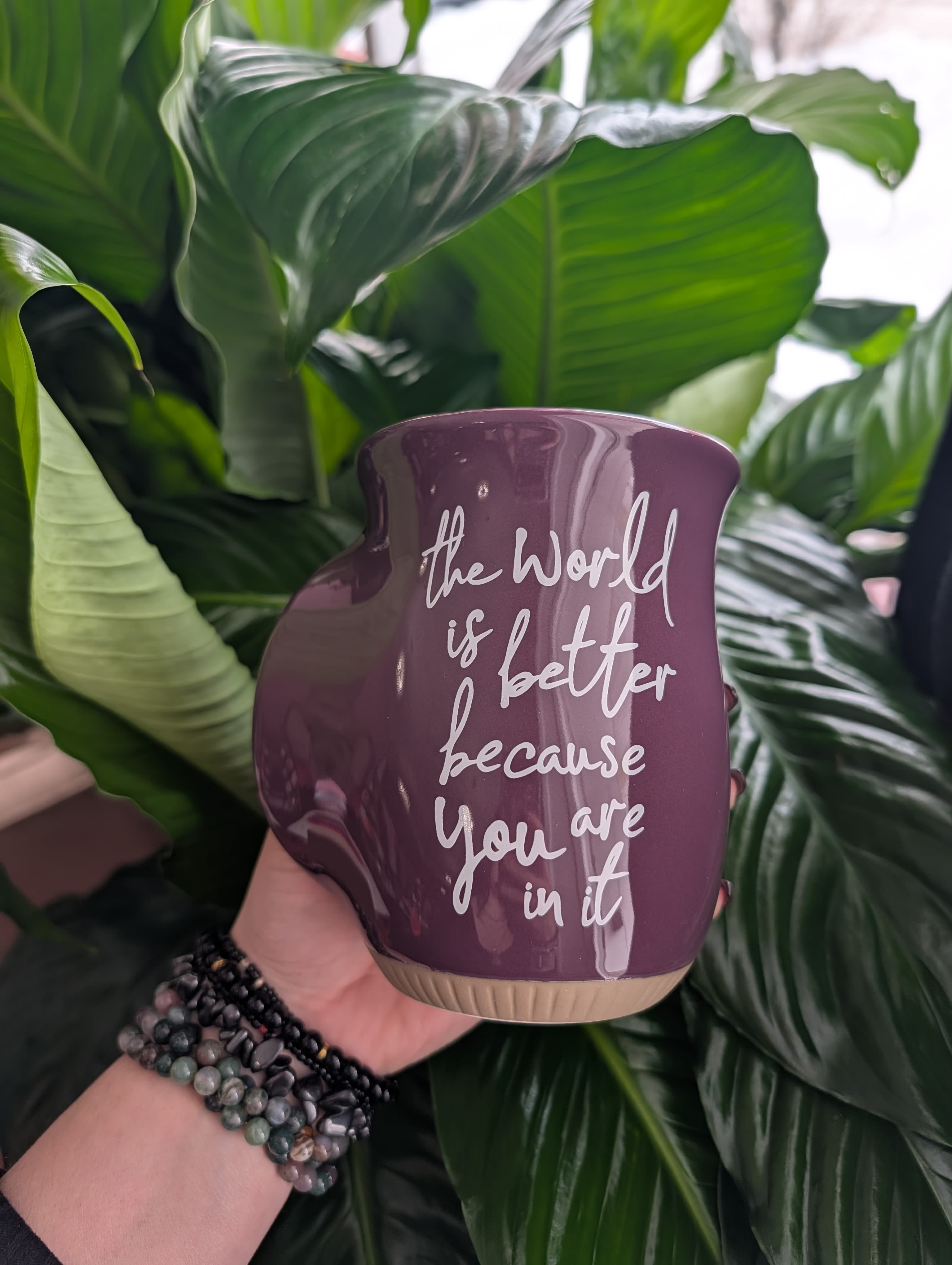 Purple ceramic planter with white text held in front of large green leaves