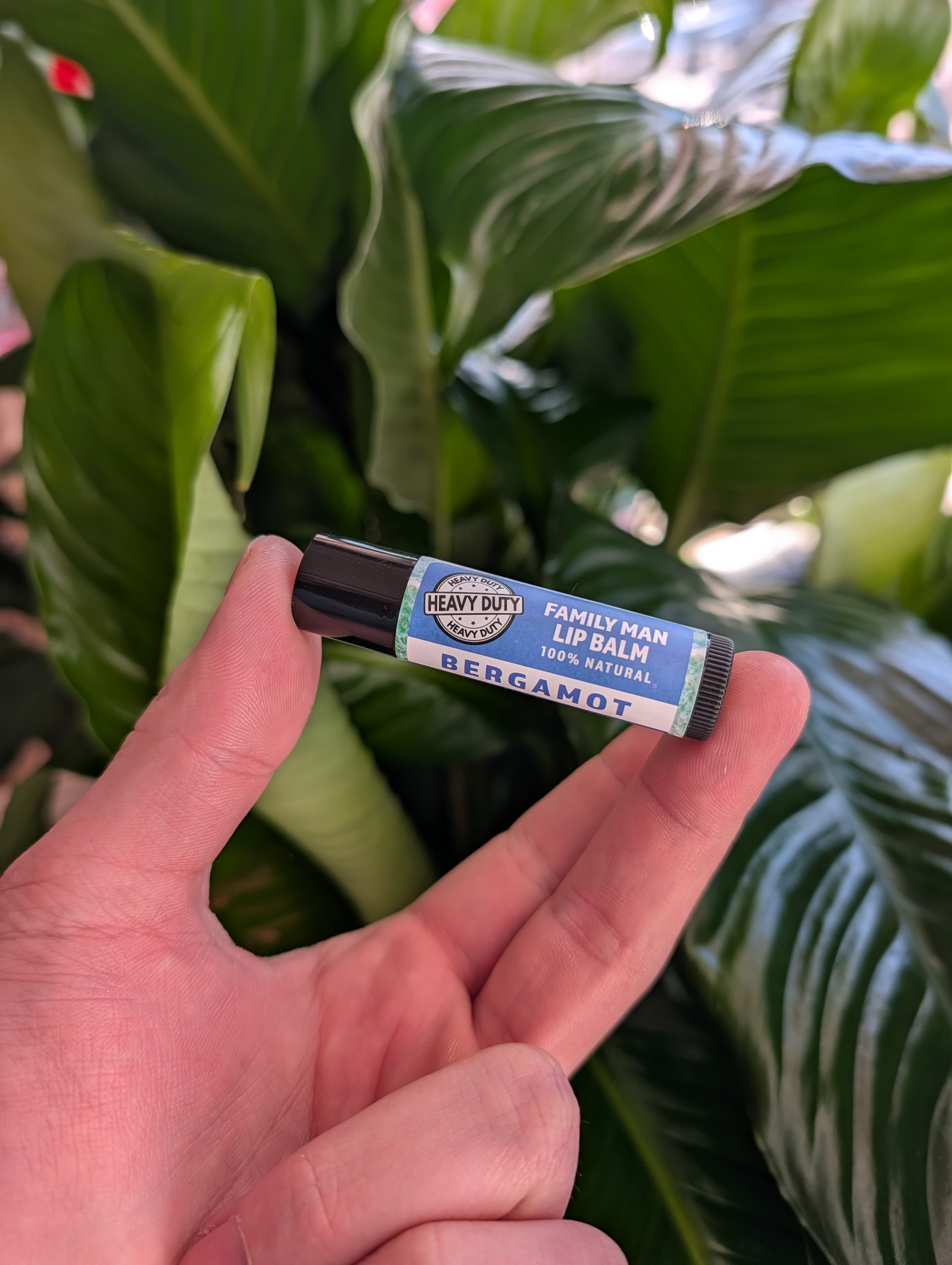 Hand holding a bergamot lip balm tube in front of green leaves