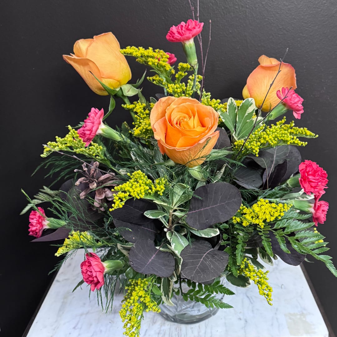 Orange roses and pink carnations in a clear glass vase