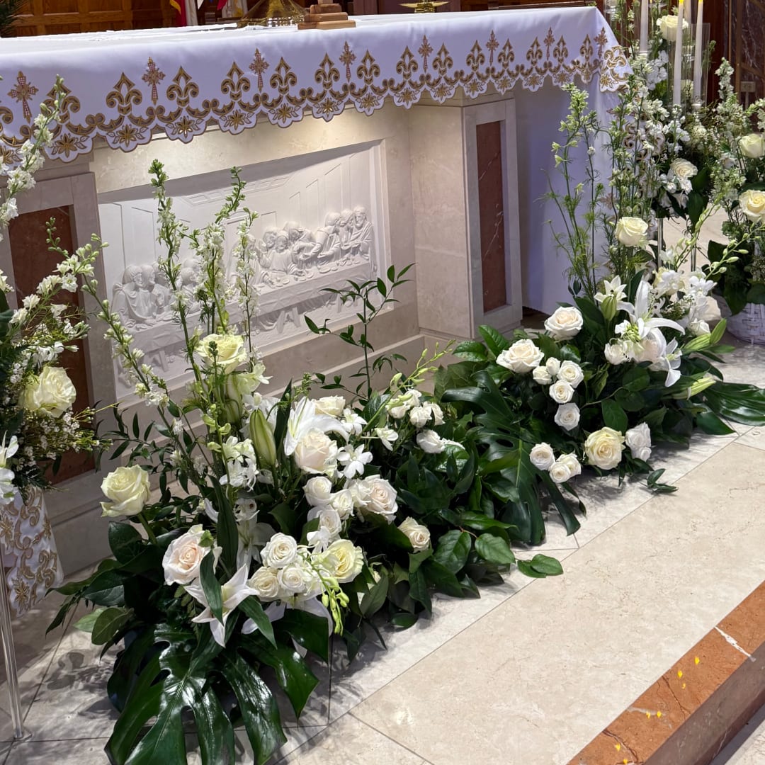 White floral arrangements with roses and lilies around an altar