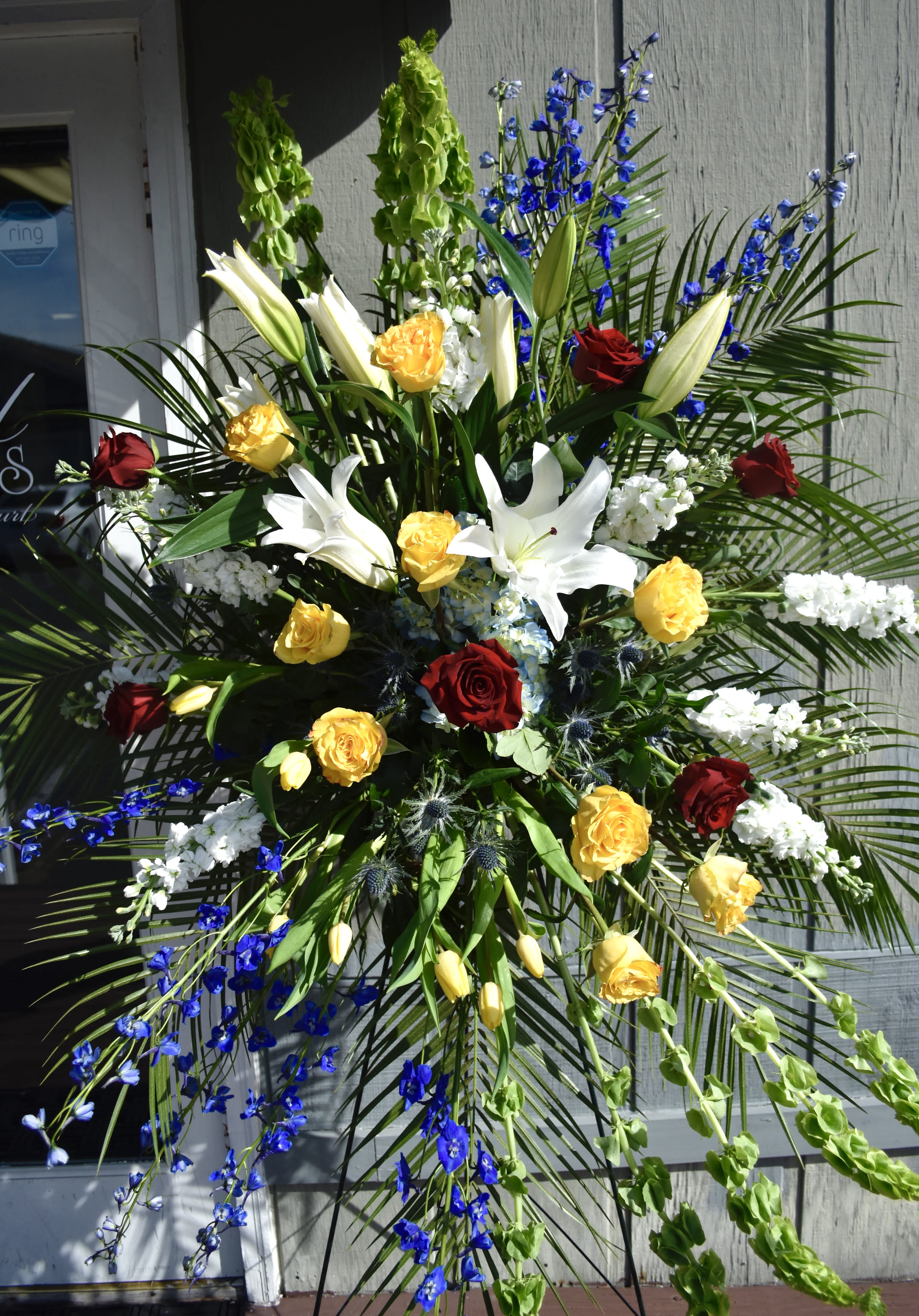 Large standing floral spray with roses, lilies, and blue flowers