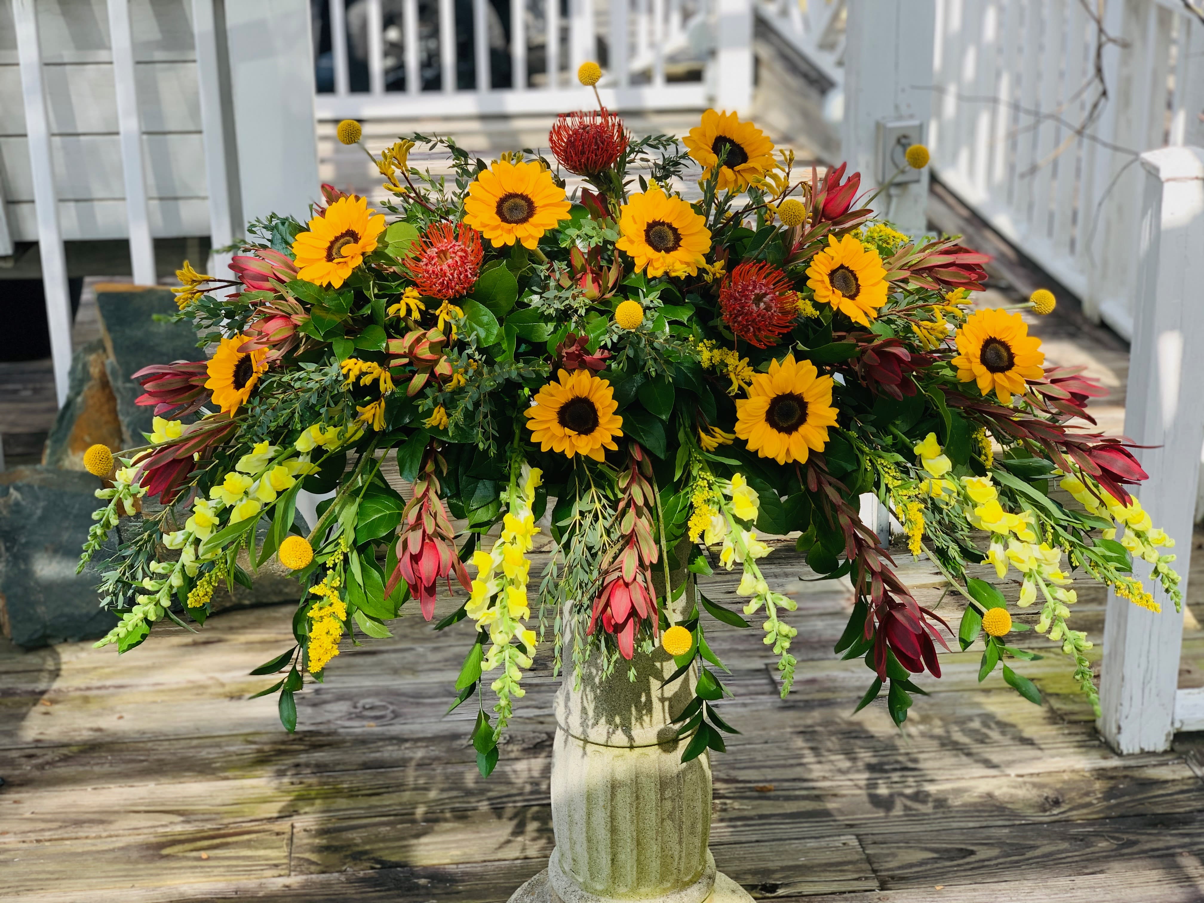 Large floral arrangement with sunflowers and red blooms in a pedestal vase