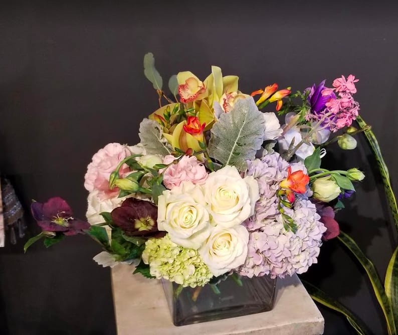 Mixed bouquet of roses, hydrangeas, and orchids in a square glass vase