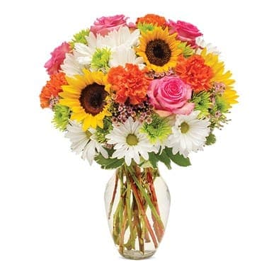 Mixed bouquet of sunflowers, daisies, roses, and carnations in a glass vase