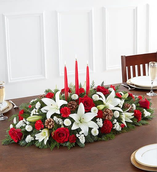 Holiday centerpiece with red candles, white lilies, and red roses on a table