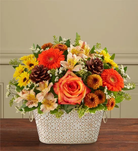 Mixed bouquet in a patterned white metal container with orange and yellow flowers