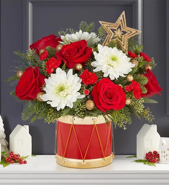 Red roses and white daisies arranged in a red drum container with a gold star topper.