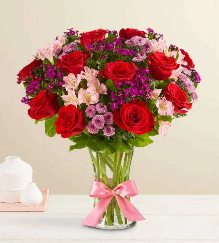 Bouquet of red roses and pink flowers in a clear glass vase with a pink ribbon