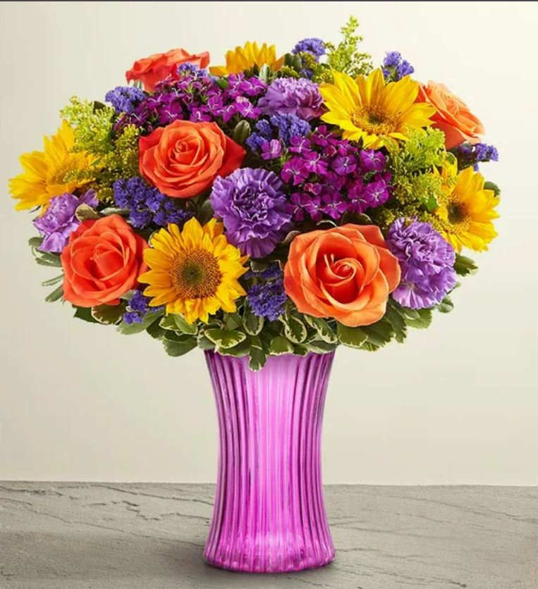 Colorful bouquet of roses, sunflowers, and purple flowers in a pink vase