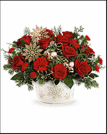 Red roses arranged in a white snowflake vase with holiday accents