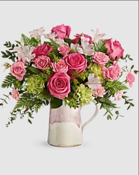 Pink roses and white flowers arranged in a glass pitcher vase